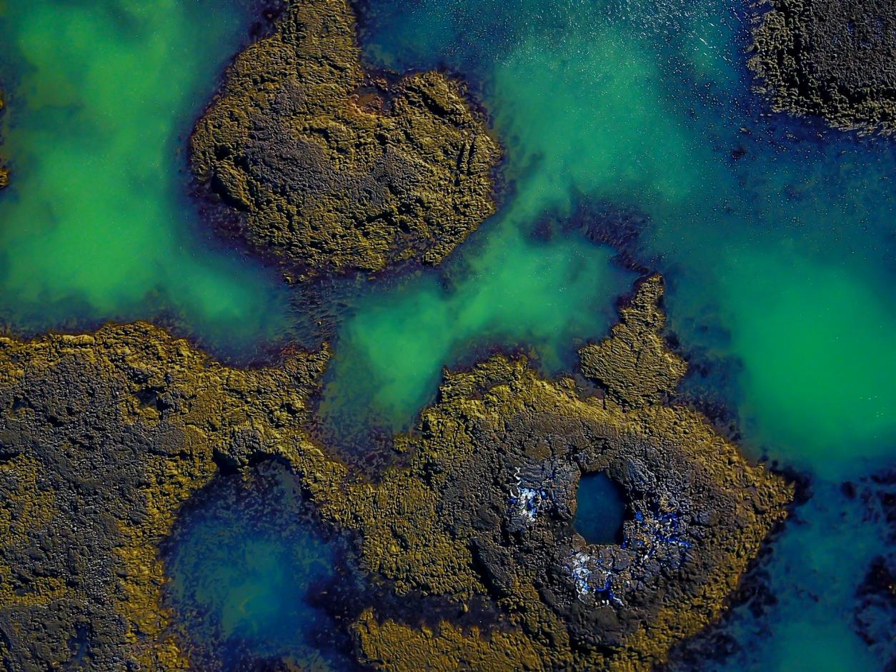 Island von oben - grünliches wasser in braunen Vulkangestein an der Küste
