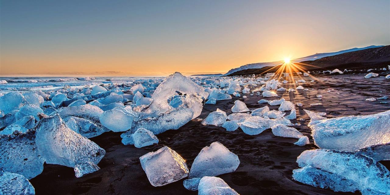 Gletschereis auf schwarzem Basaltsand am Meer im Gegenlicht der Abendsonne